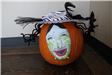 A pumpkin wearing a white-and-green witch's mask, a zebra-striped witch's hat and black stream