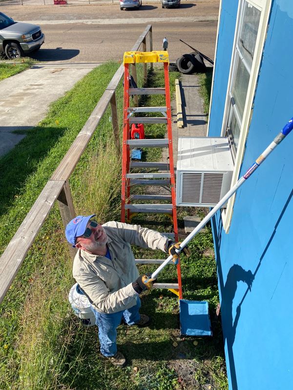 Man with sunglasses painting a house blue with a long paint roller