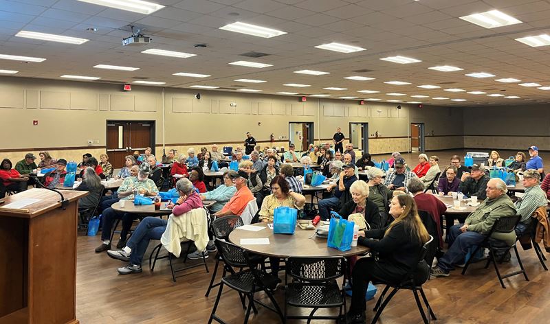 Large group of people seated at round tables in the Community Center annex