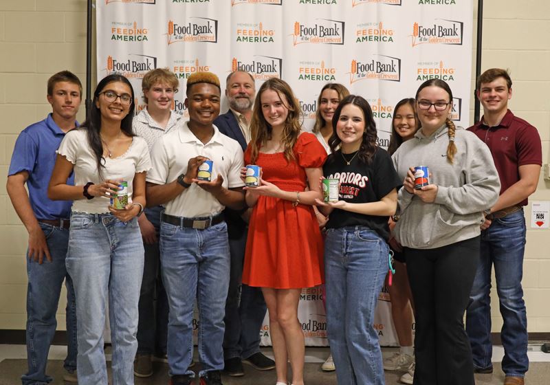 Group picture of mayor and several teenagers holding cans in front of a food bank backdrop