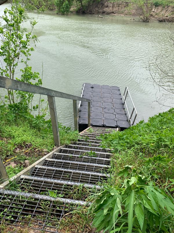 A boating ramp with metal stairs leading down to a black rubber or plastic floating ramp