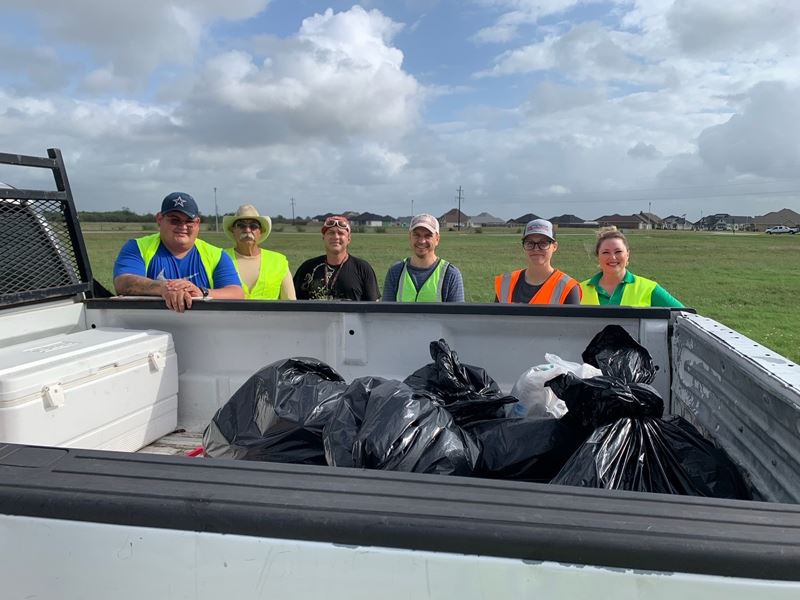Six people pose for a photo with bags of trash in a truck bed
