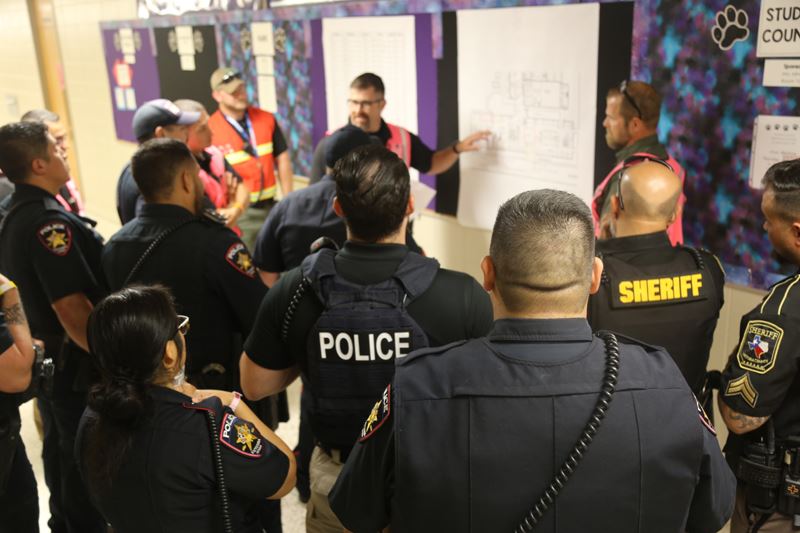 Victoria Police Department and Victoria Sheriff's Office personnel stand in a hallway at a school