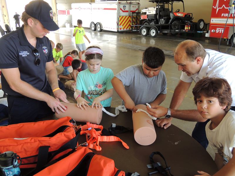 Firefighters help kids place white bandages on dummy limbs
