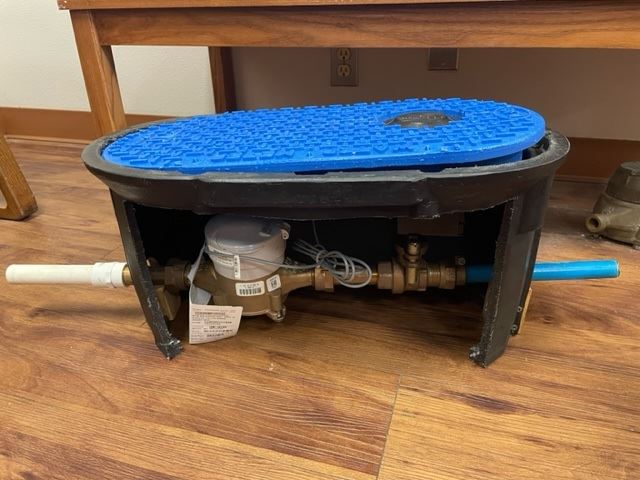 A water meter with a blue lid on top. The side is cut open to show pipes and wiring.