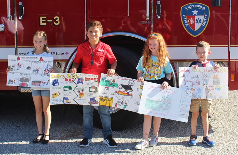 Four children holding handmade posters in front of a fire truck