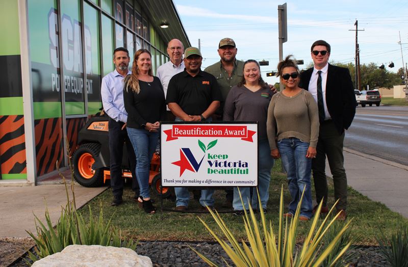 Group photo with KVB sign in front of a business with rocky flowerbed in the foreground