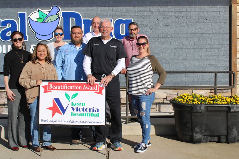 Group photo with Keep Victoria Beautiful sign next to planter filled with yellow flowers