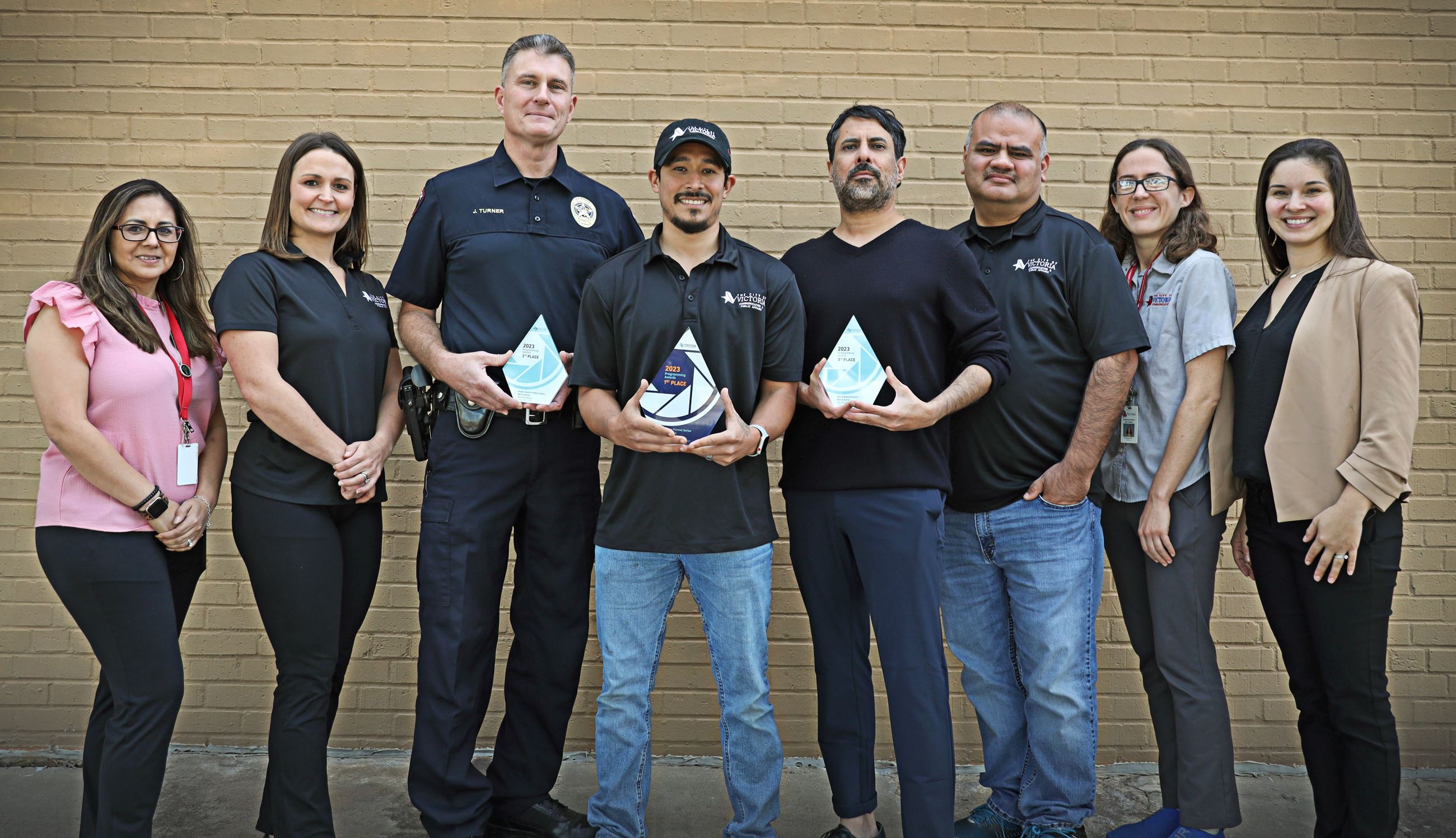 eight people standing in front of a brick wall. the middle three are holding an award