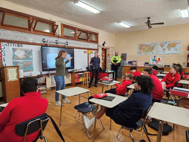 Three people standing and in front of a class of children.