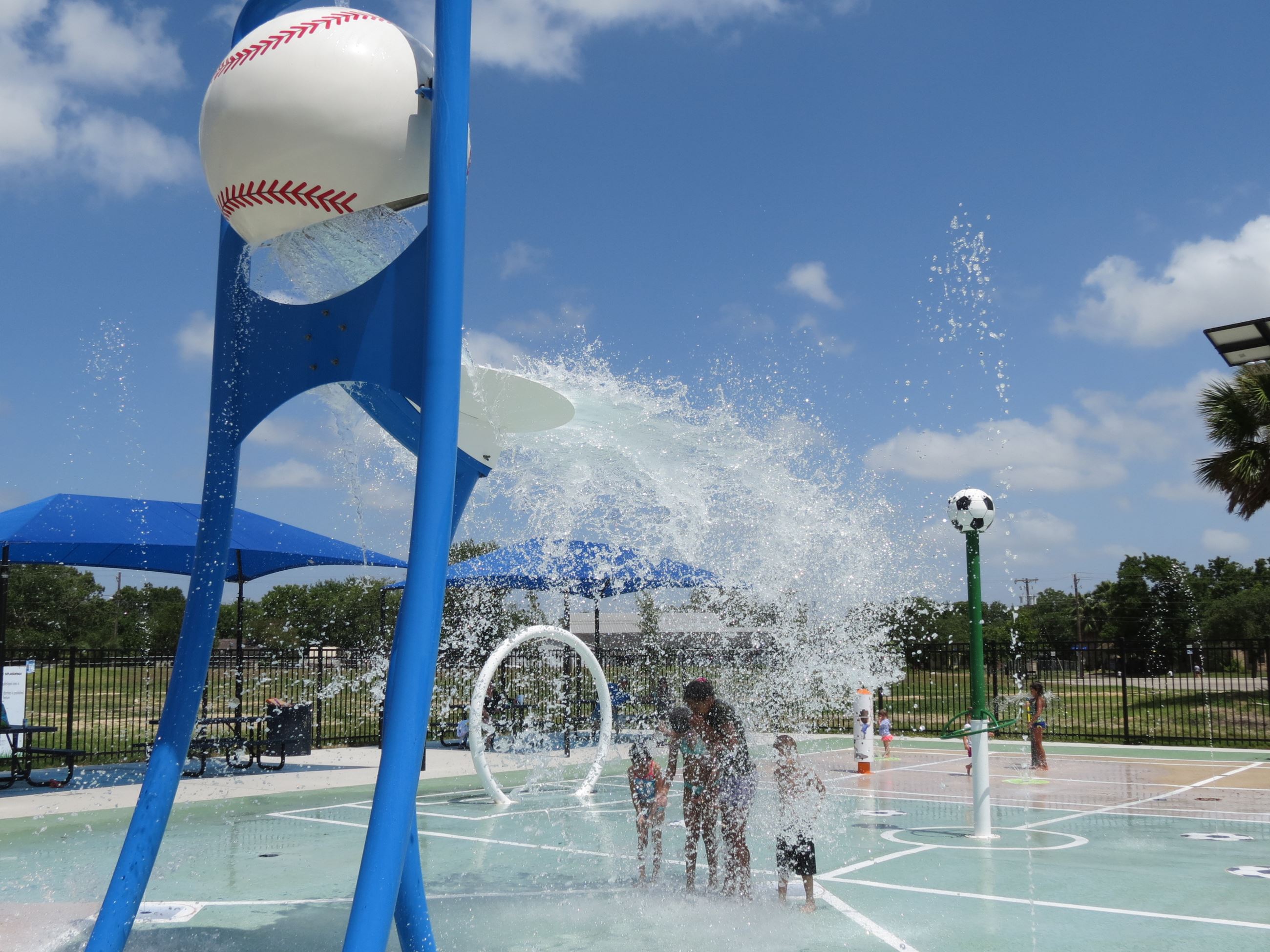 Four people getting splashed my water coming out of an oversized baseball