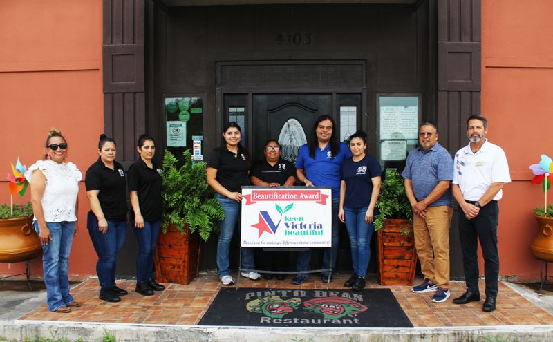 Group photo in front of Pinto Bean with potted ferns and a welcome mat with Pinto Bean logo