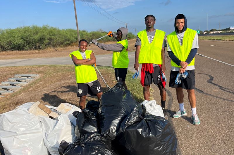 Young men in safety vests pose with bags of trash