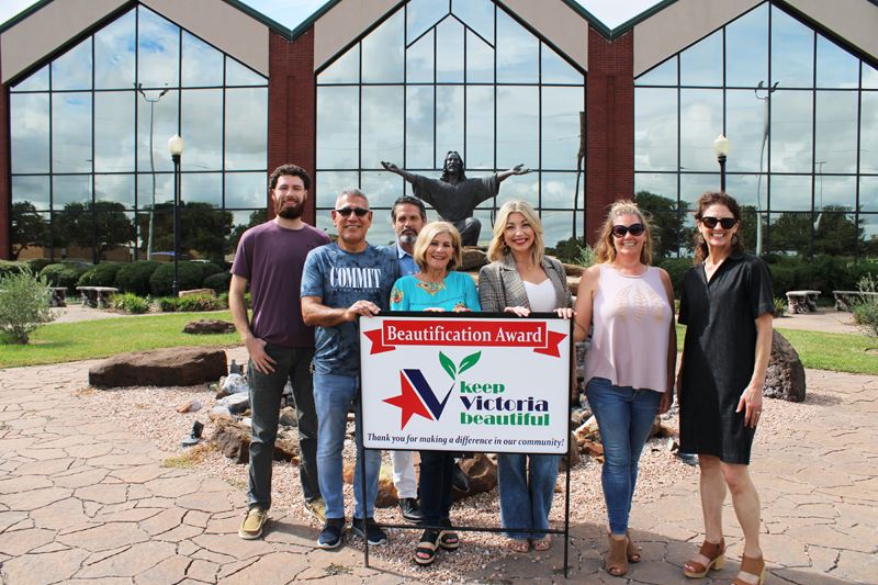 Group photo with KVB sign in a courtyard with a Jesus statue and decorative rocks and foliage