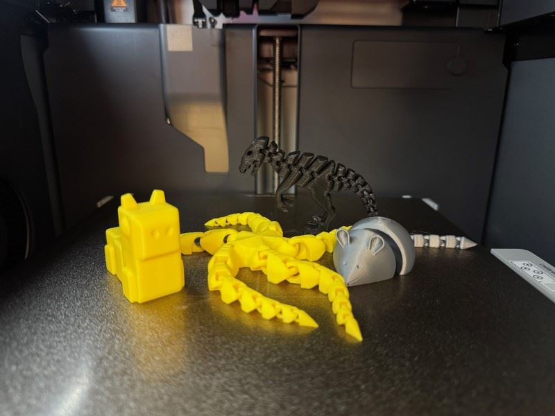 Four items created from a 3D printer including an articulated mouse, dinosaur, starfish, and a robot