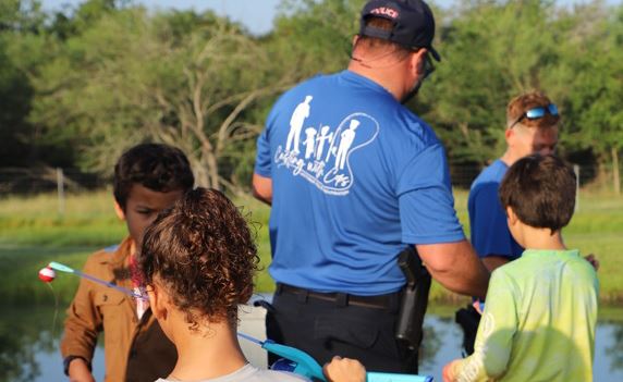 A man in a Casting with Cops shirt and several children with fishing poles on a pier