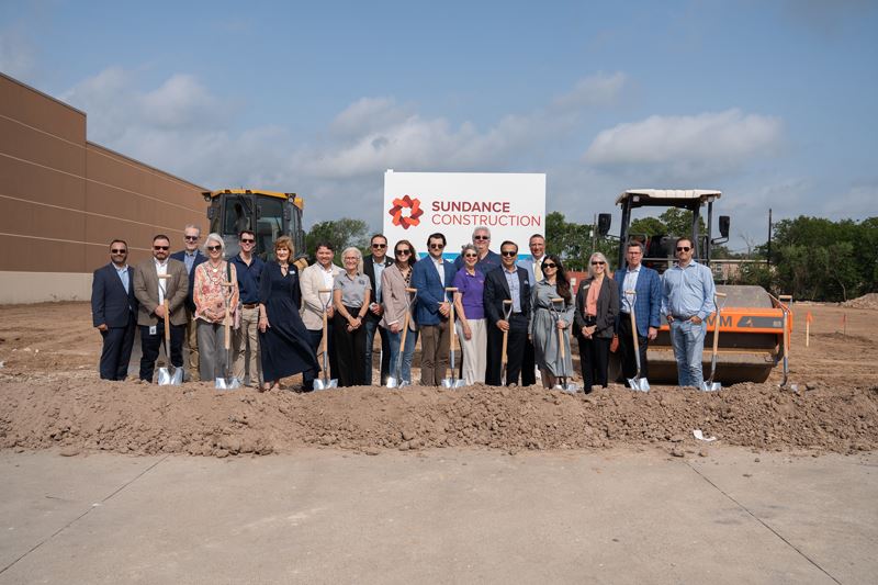 Large group photo with shovels in front of a Sundance Construction sign with ground being levelled 