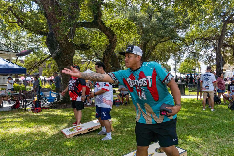 Cornhole competition at De Leon Plaza. A man tosses a bean bag near the gazebo