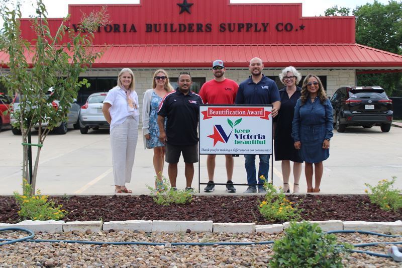 Group photo with KVB sign by a plant bed with flowering shrubs, small trees and volcanic rocks