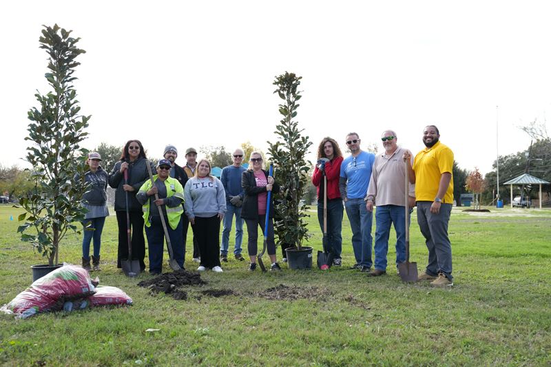 12 people pose for a photo with shovels and potted trees in Pine Street Park