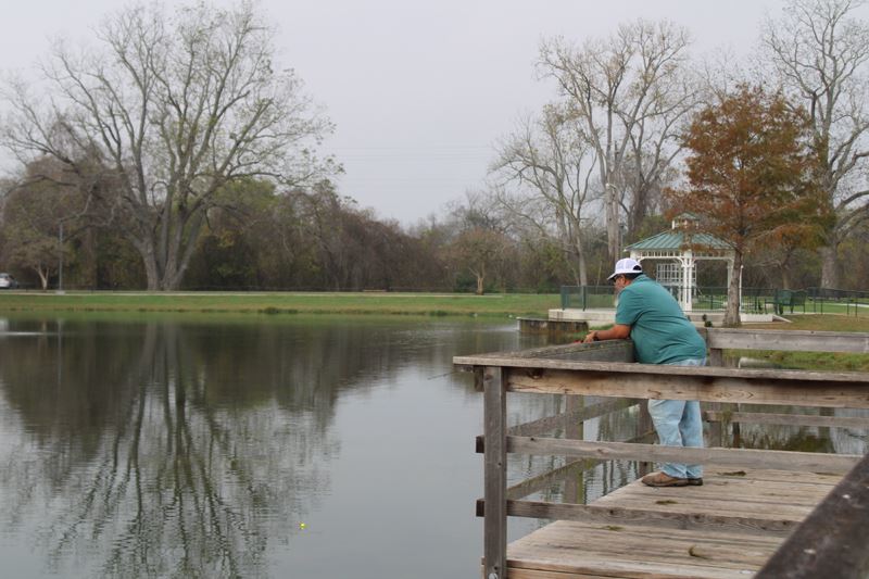 A man in a ball cap casts a fishing line off the boardwalk at the Riverside Park duck pond