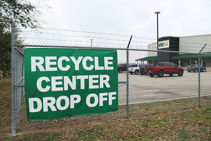 A Waste Management facility with a sign for recycle center drop off posted on a chain link fence