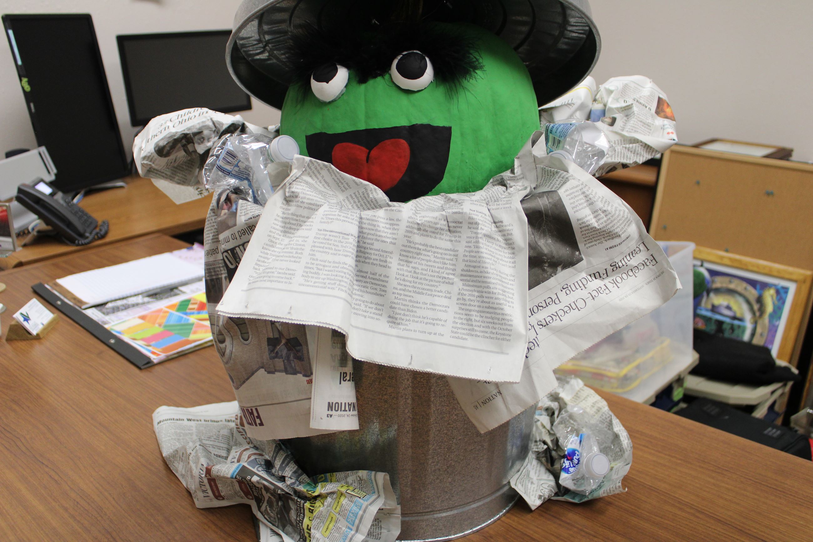 Oscar the Grouch figure in trash can with pumpkin for head. Trash, papers scattered around base