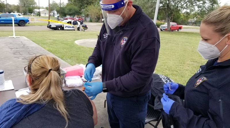 Fire department employee gives a woman a flu shot in an outdoor park.
