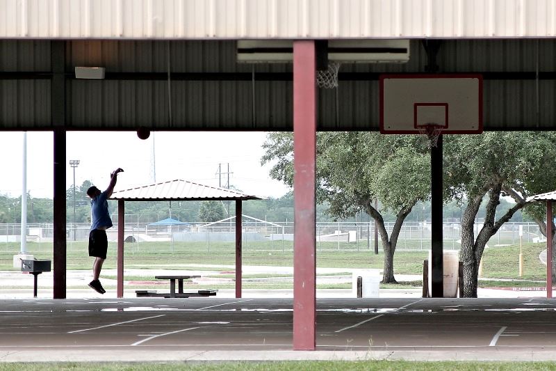 A silhouetted basketball player shoots a basket at an empty basketball court.