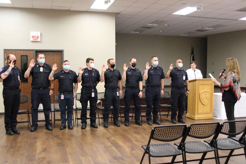 Five people in firefighter dress shirts raise their hands as they are sworn in by a woman