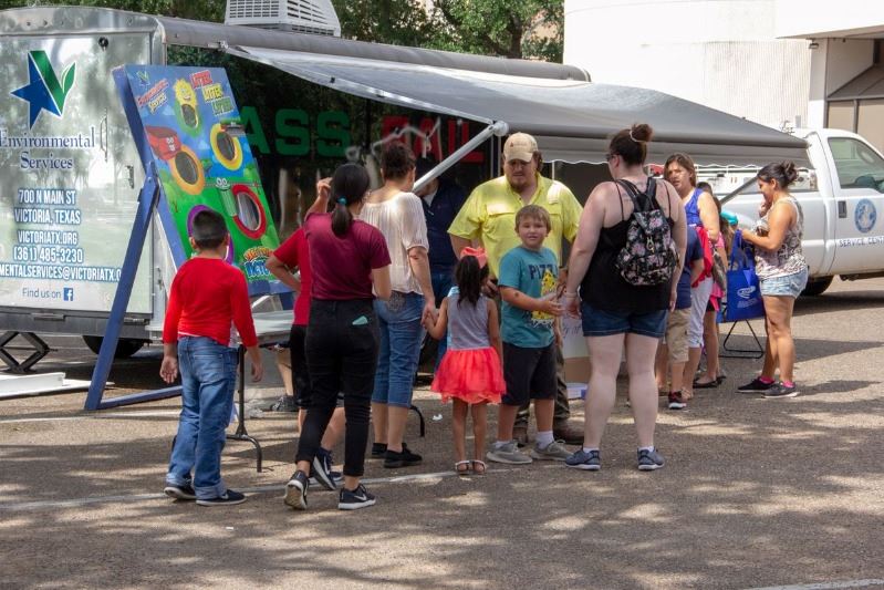 Families wait outside activity trailer that has an Environmental Services logo and bean bag toss.