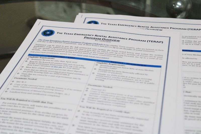 Application forms for the Texas Emergency Rental Assistance Program stacked on a glass side table.