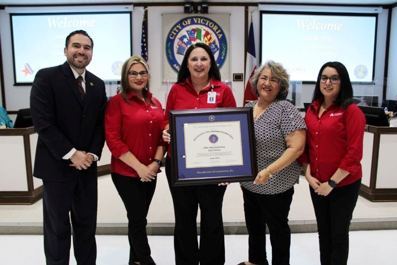 Five people pose with a framed certificate at the City Council chambers.