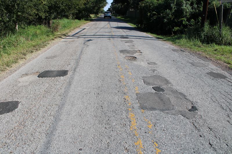A rural roadway covered in patches, cracks and potholes