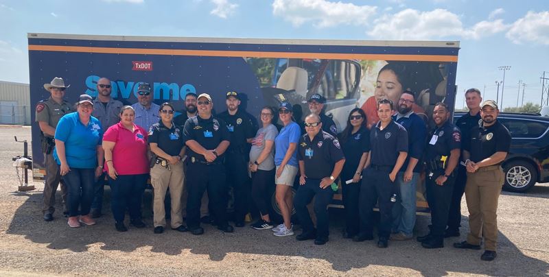 Group photo of people in different uniforms standing in front of a TxDOT trailer