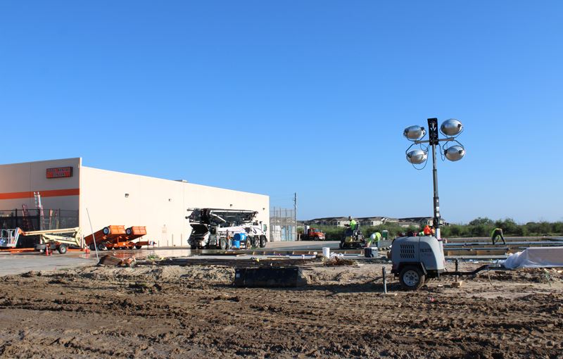 Construction crew laying a concrete foundation next to Home Depot. Machinery and lights are present.