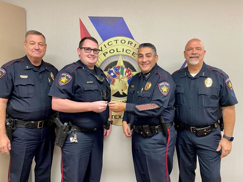 Four uniformed police officers. Man second from right hands a small object to man second from left