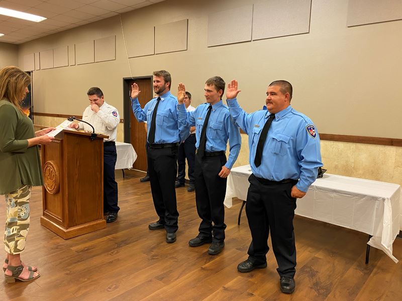 Three people in firefighter dress shirts and ties raise their hands during a swearing in ceremony