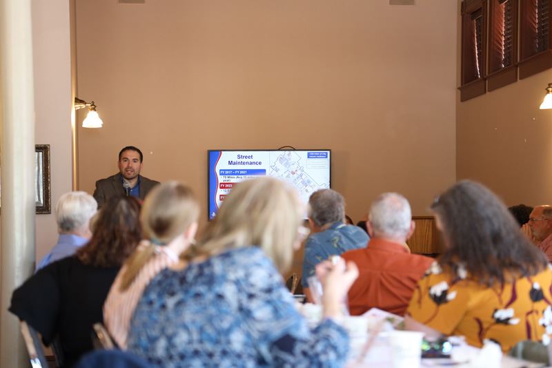 A man holding a microphone stands next to a screen with a map labeled Street Maintenance.