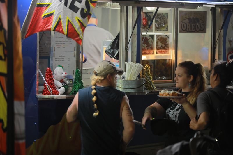 People standing in line at a food truck. A woman holds a funnel cake.
