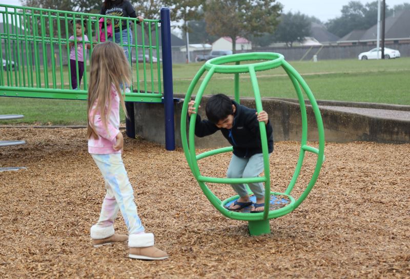 A small boy climbs on a green spinning structure while a girl watches him