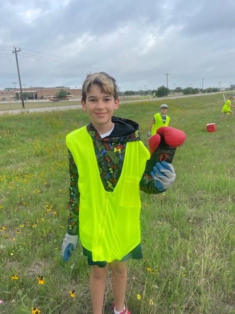 A boy in a yellow work vest in a field holds a boxing glove