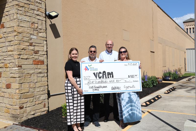 Group photo with a giant check in front of landscaping at the VCAM building