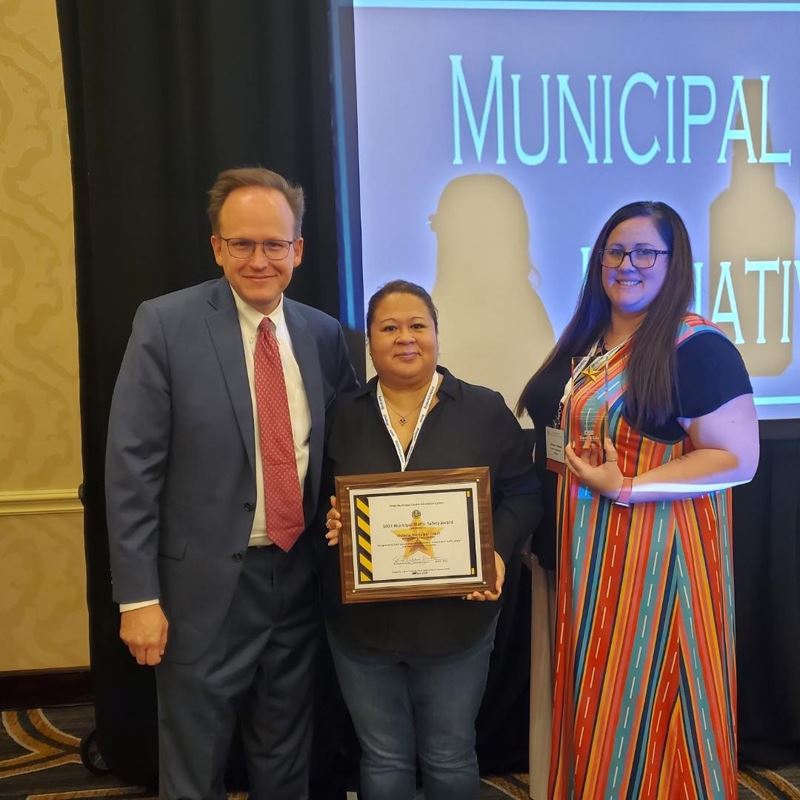 Three people pose for a photo. One holds a plaque and one holds a small glass trophy.