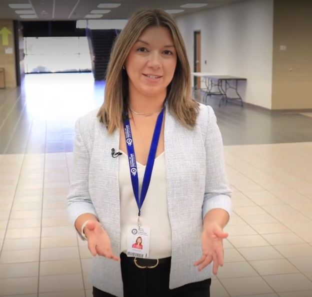 A woman in a blue lanyard walks through a wide empty school foyer