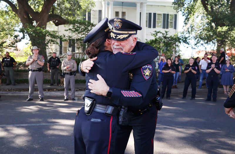 Deputy Chief Mark Jameson hugs Deputy Chief Eline Moya while people applaud in the background