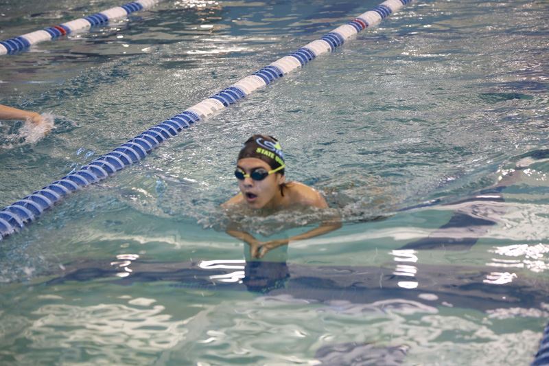 A person with goggles and a swim cap swimming in a pool.