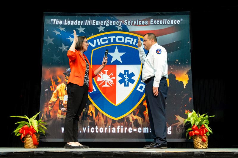 Man in firefighter dress uniform raises his hand as he is sworn in by a woman near VFD backdrop