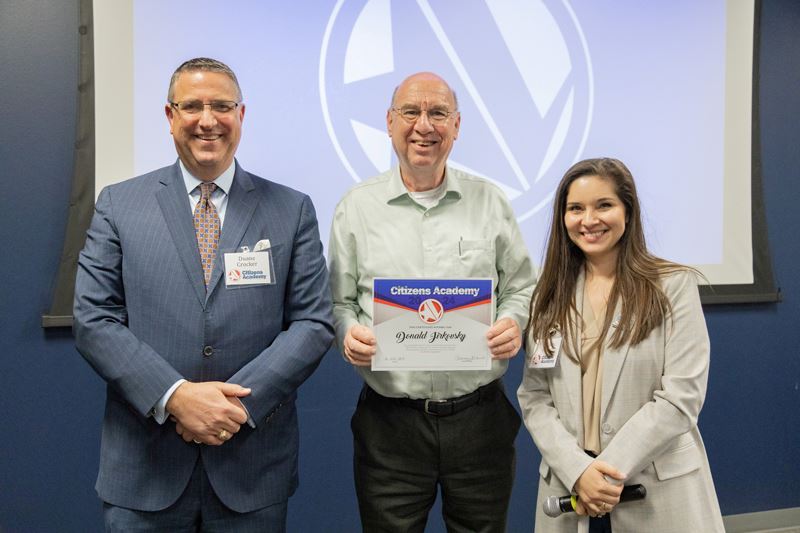 Three people in a group photo. The man in the middle holds a certificate.