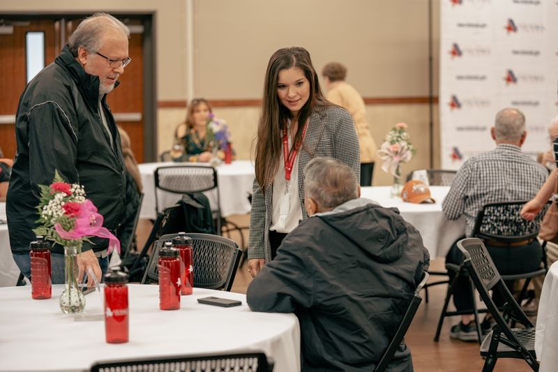A woman stands near a table talking to two men